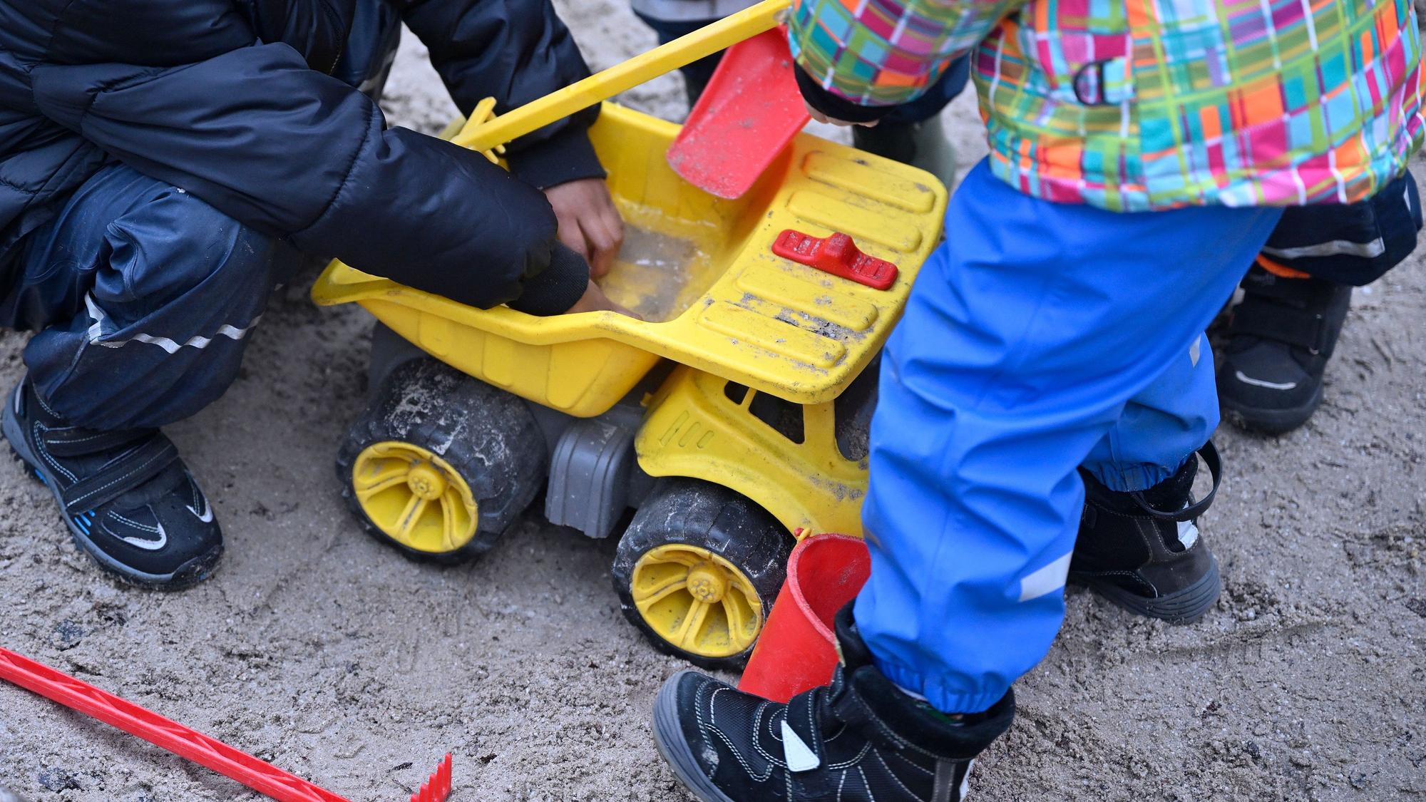 Kinder spielen mit einem gelben Spielzeugbagger im Sand.