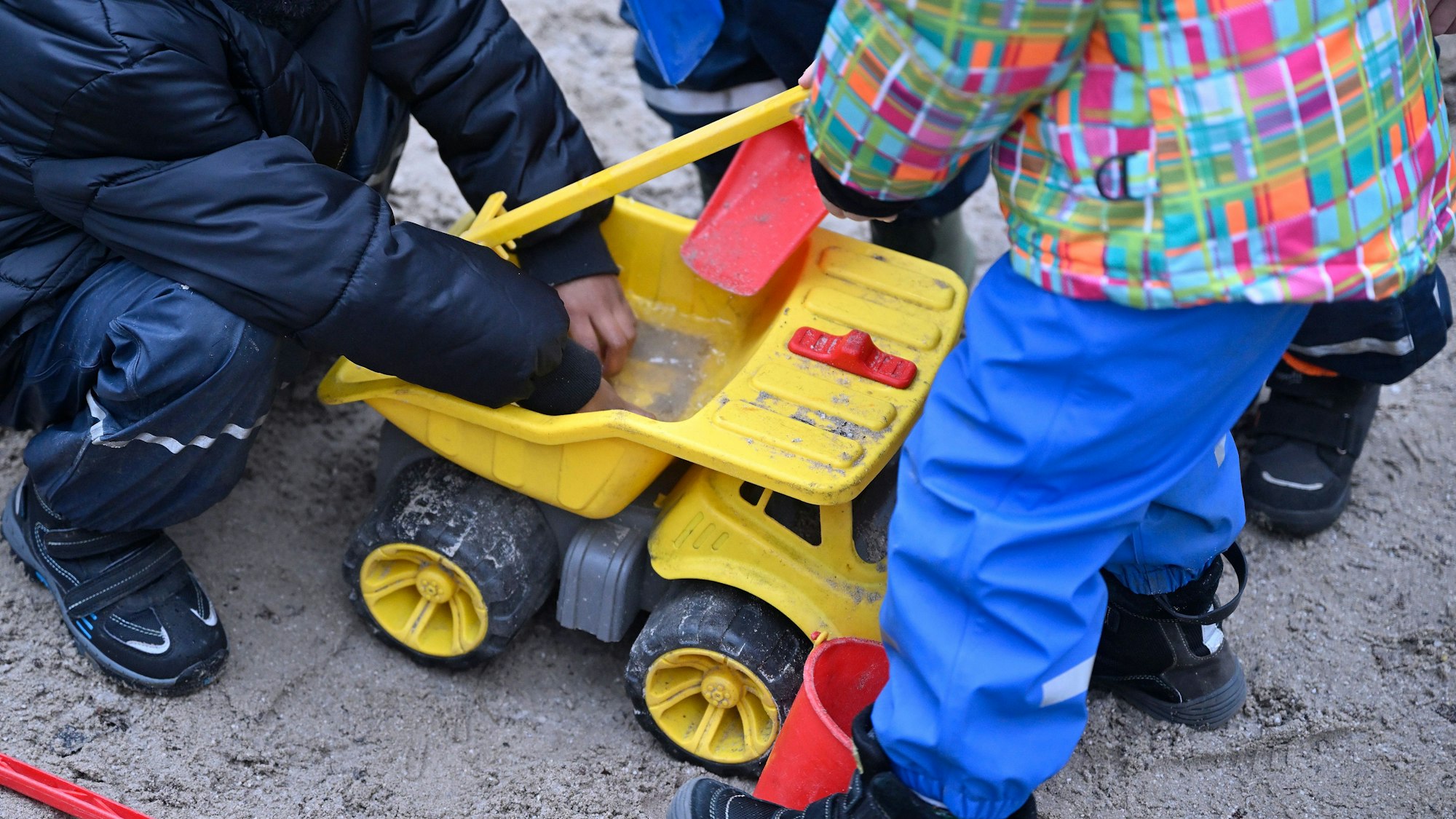 Spielende Kinder im Sandkasten eines Kindergartens.