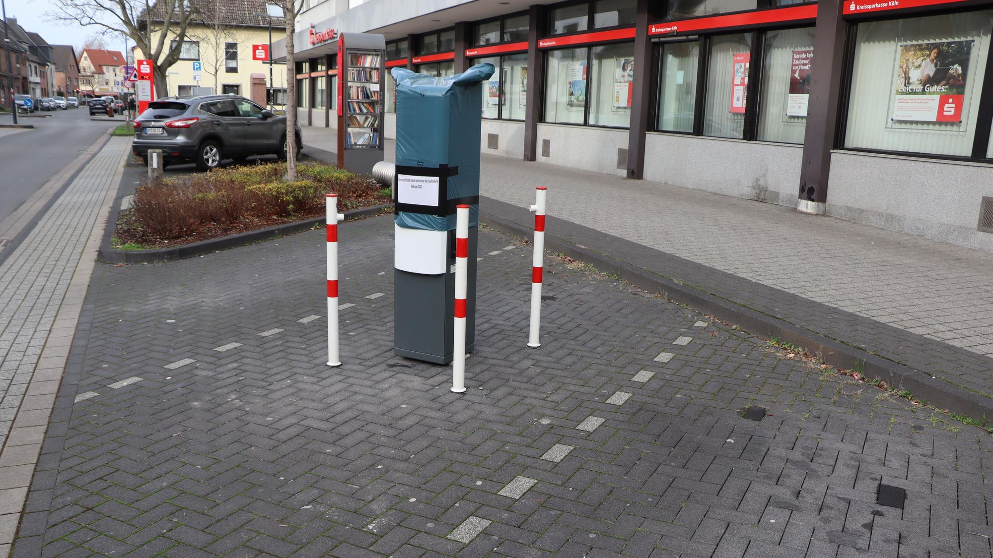 Mitten auf einer Parktasche wurde eine E-Ladesäule montiert. Drumherum stehen rot-weiße Poller.
