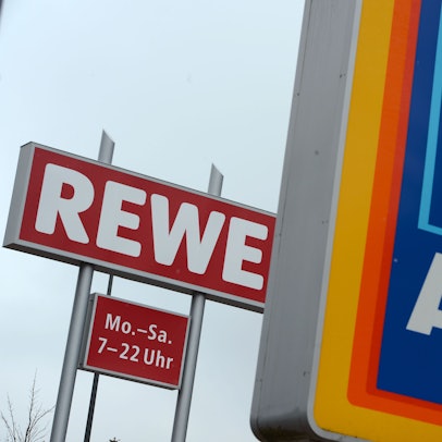 Schilder des Discounters Aldi Süd und der Supermarktkette Rewe stehen an der Zufahrt eines Industriegebiets in Glashütten (Hessen).