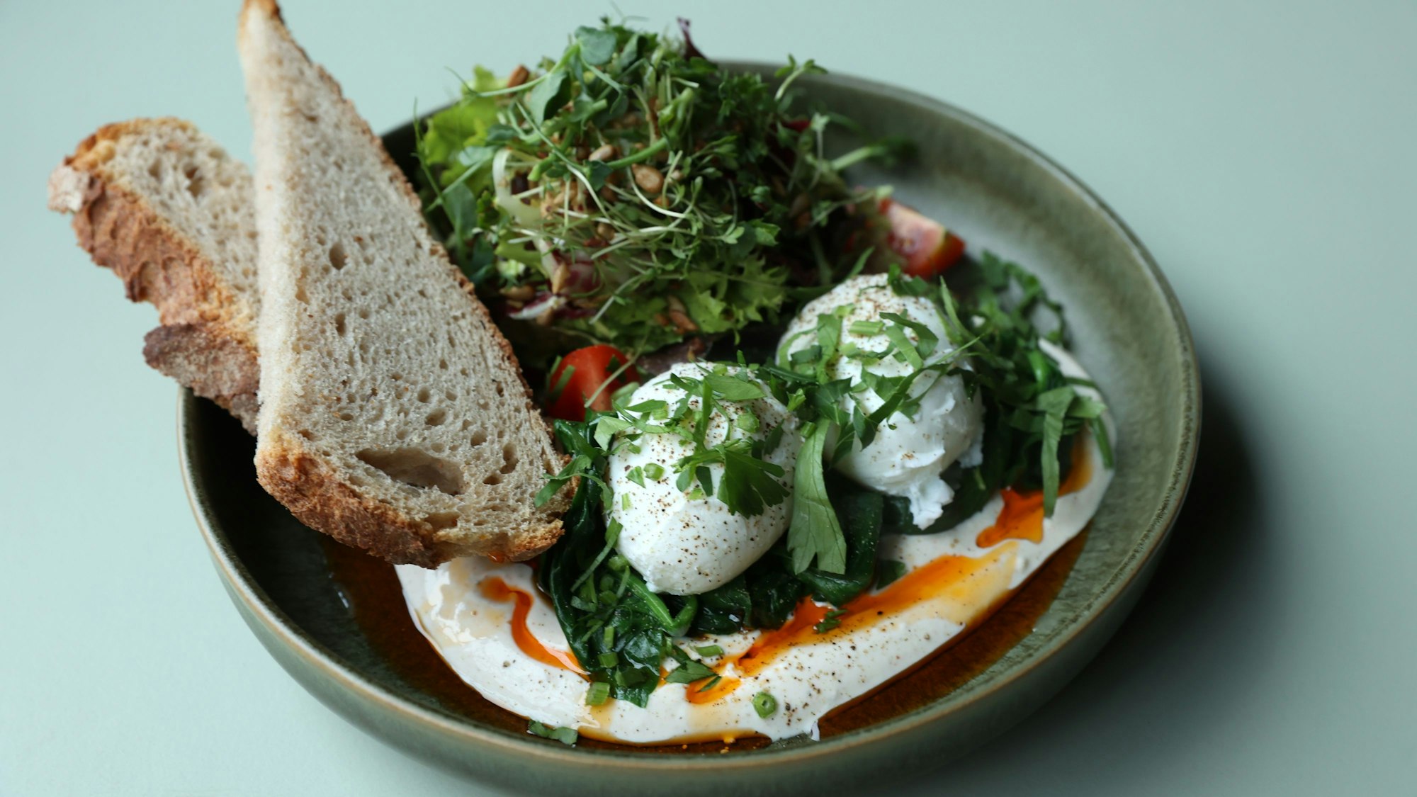 Shakshuka, zwei pochierte Eier mit Tomate, Paprika, Feta und Landbrot appetitlich angerichtet auf einem Teller