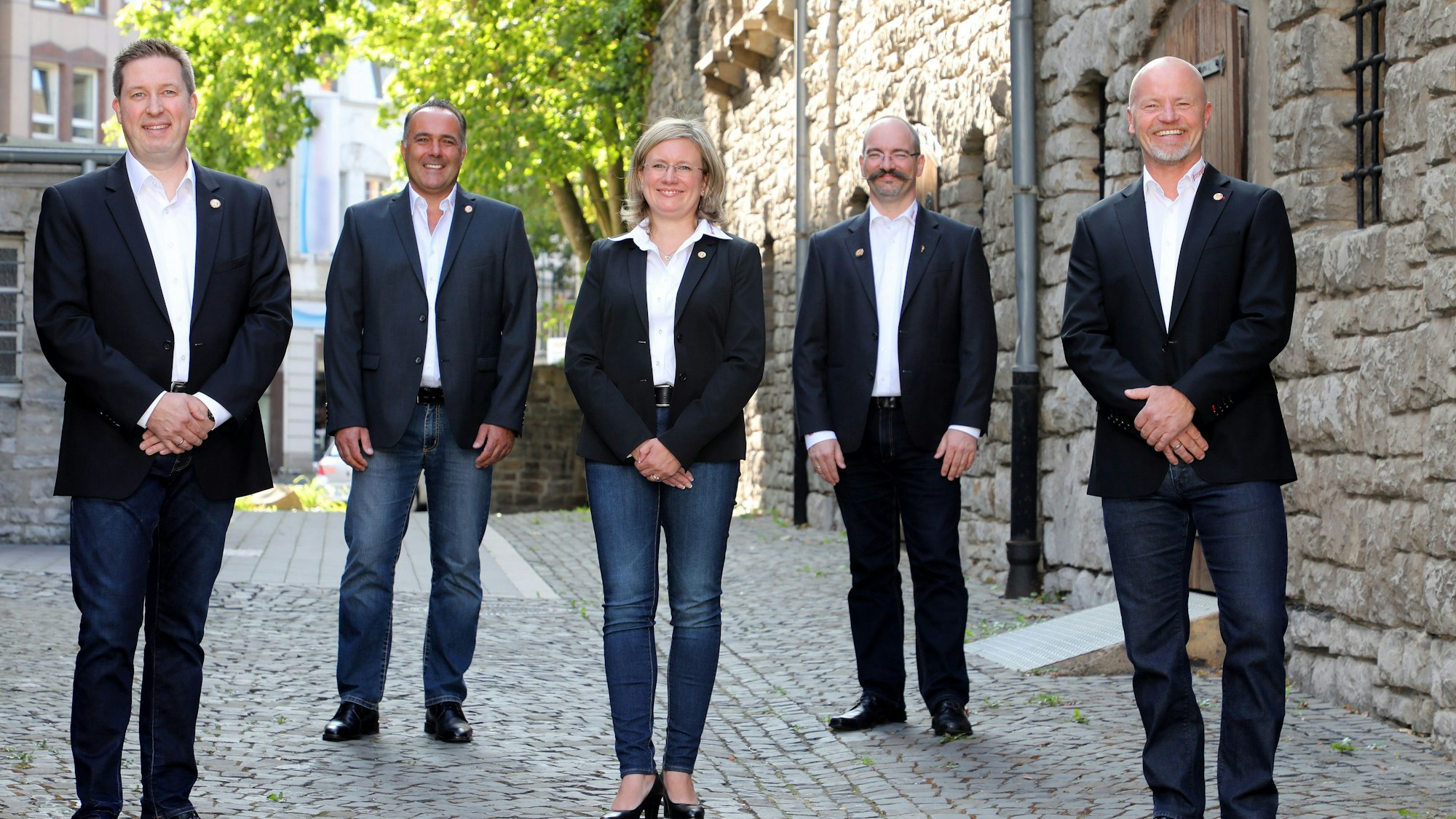 Das Dreigestirn und zwei aus dem Gefolge stehen in schwarzen Sackos hinter dem Rathaus.