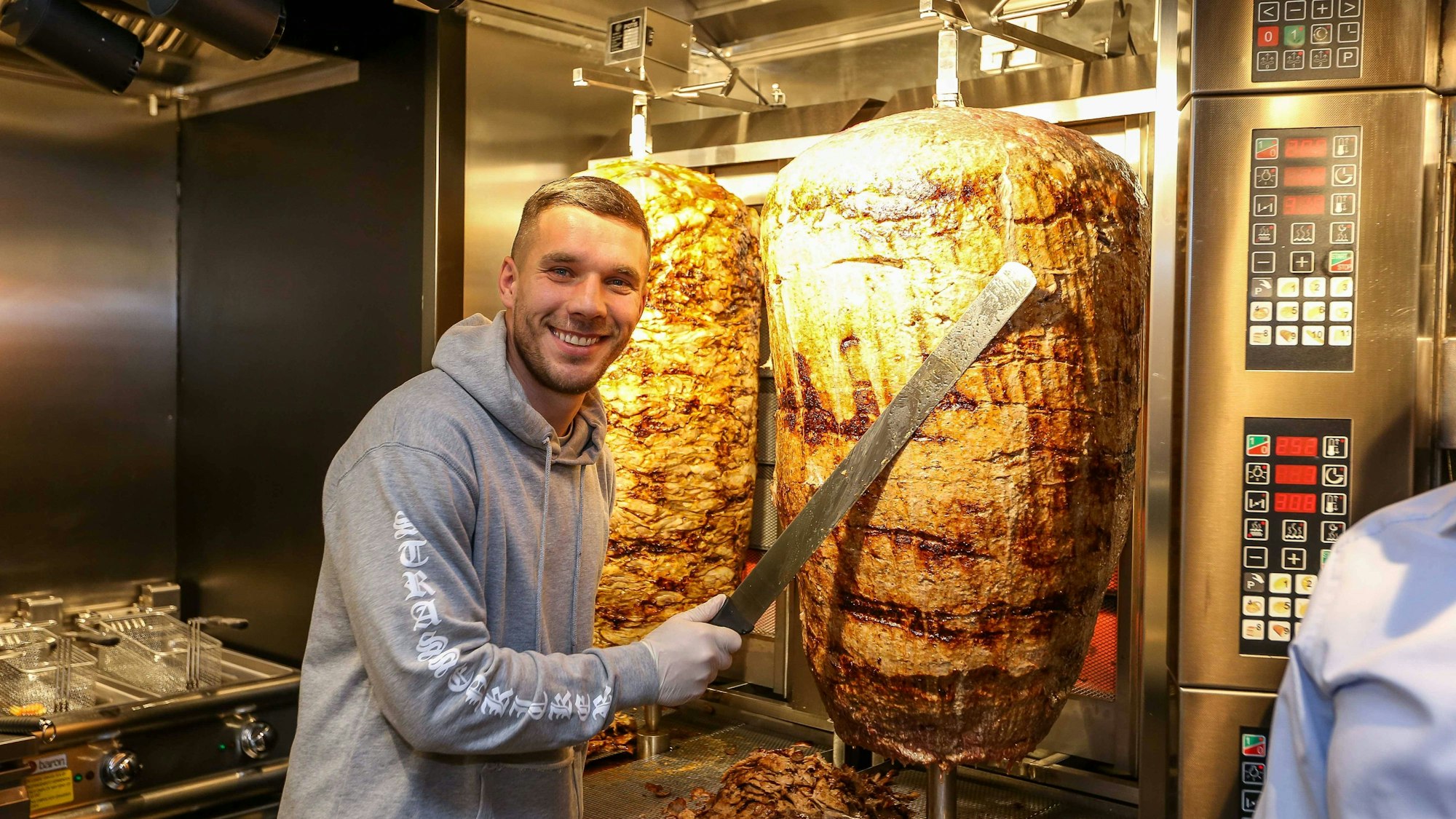 Fußball-Weltmeister Lukas Podolski posiert bei der Eröffnung eines Mangal-Döner-Ladens 2018 an einem Dönerspieß.