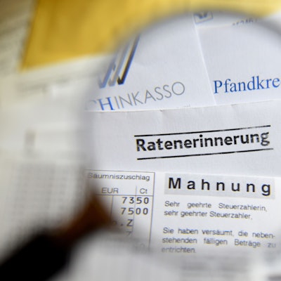 Durch eine Lupe sind Briefe und Dokumente mit Mahnungen, Ratenerinnerung, Pfandkredit, Inkasso und gelbe Briefe vom Gerichtsvollzieher zu sehen.