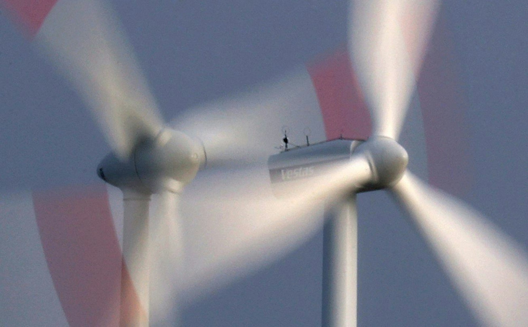 Zwei Windräder drehen sich bei heftigem Wind vor bewölkten Himmel.