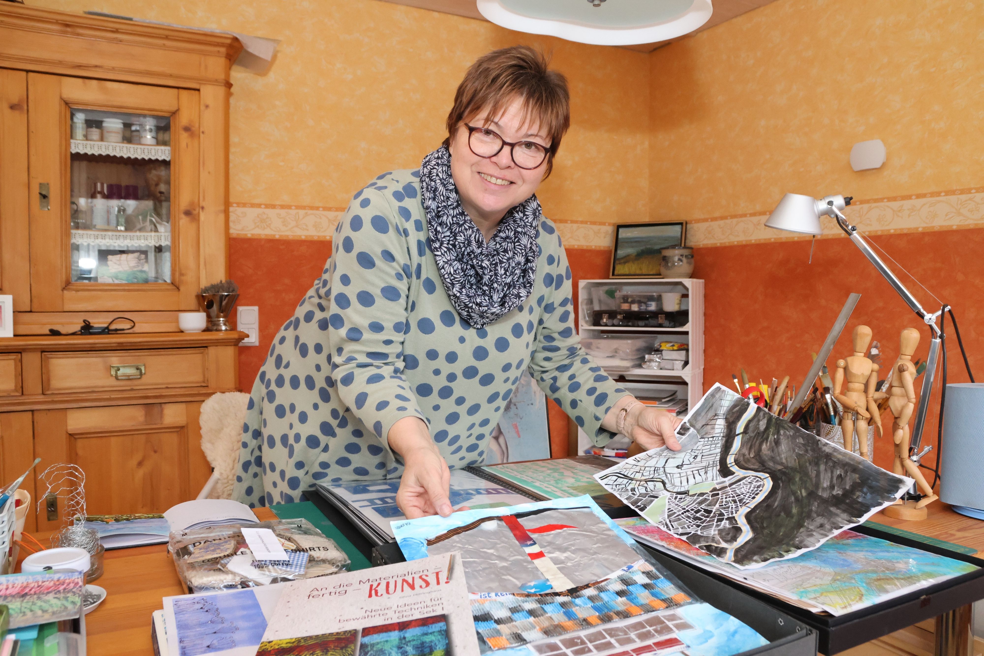 Die Autorin Silvia Hillringhaus an einem Tisch mit Malereien.