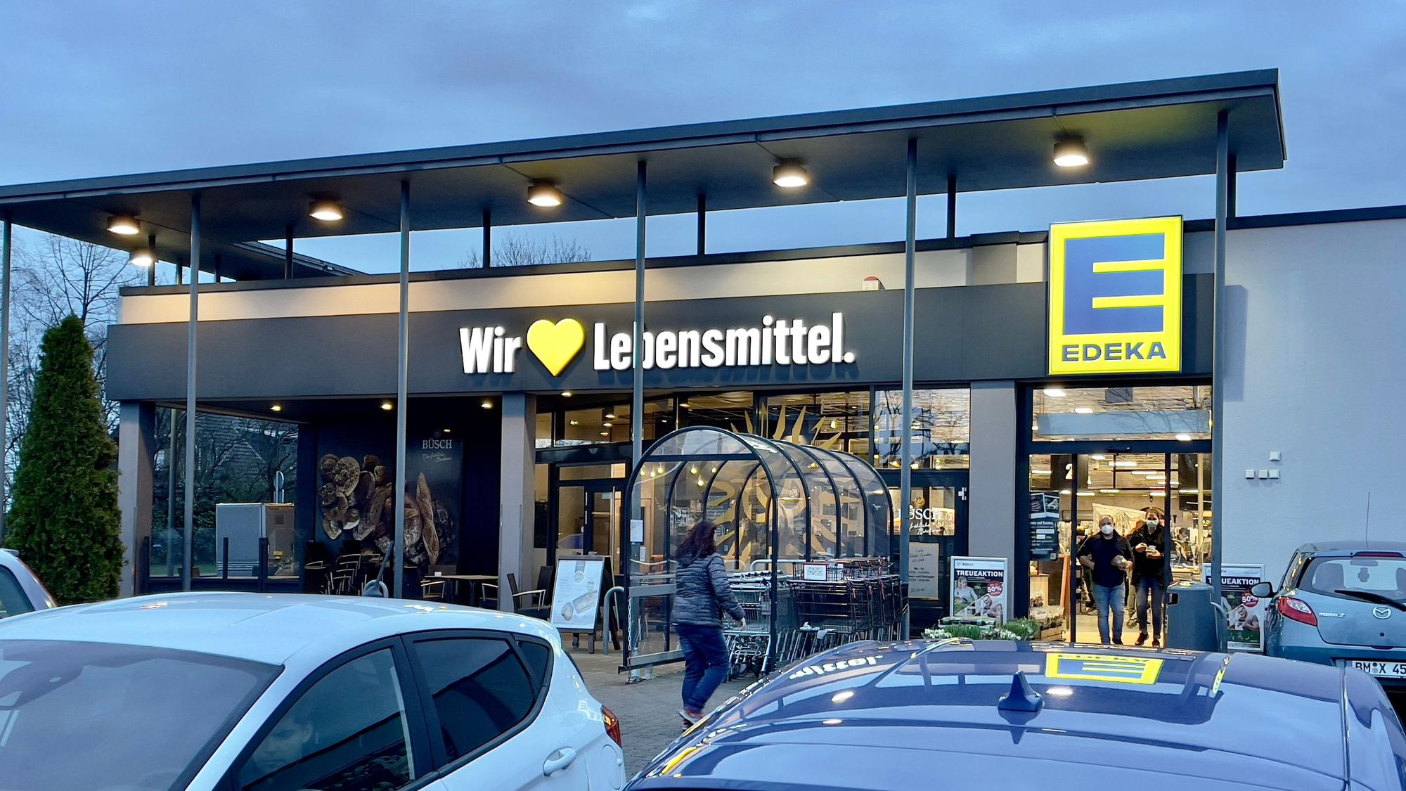 Der Eingang einer Edeka-Filiale mit parkenden Autos im Vordergrund.
