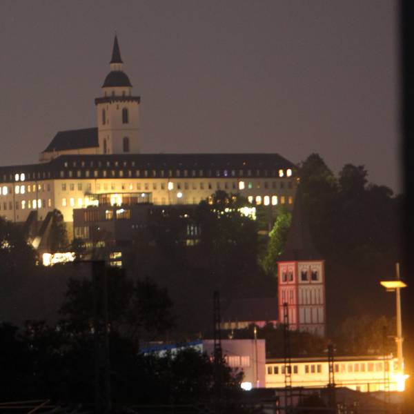 Vor dem nächtlichen Himmel hebt sich die erleuchtete Abtei auf dem Michaelsberg ab, der Turm der Kirche ragt in die Höhe. Weiter unten steht die rot-weiße Servatiuskirche.