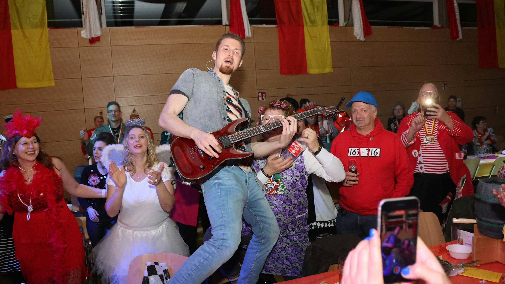 Ein Mann steht bei einer Karnevalssitzung mit einer Gitarre auf einem Tisch.