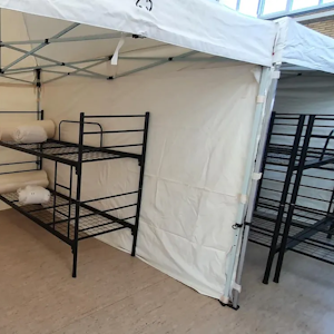 Das Foto zeigt eine Turnhalle in Frechen, in der Geflüchtete wohnen. In Zelten befinden sich jeweils zwei Doppelbetten.