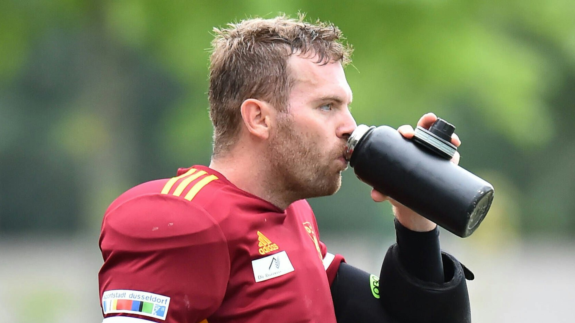 Ein Hockeytorhüter trinkt mit gedankenverlorenem Blick aus seiner Flasche.