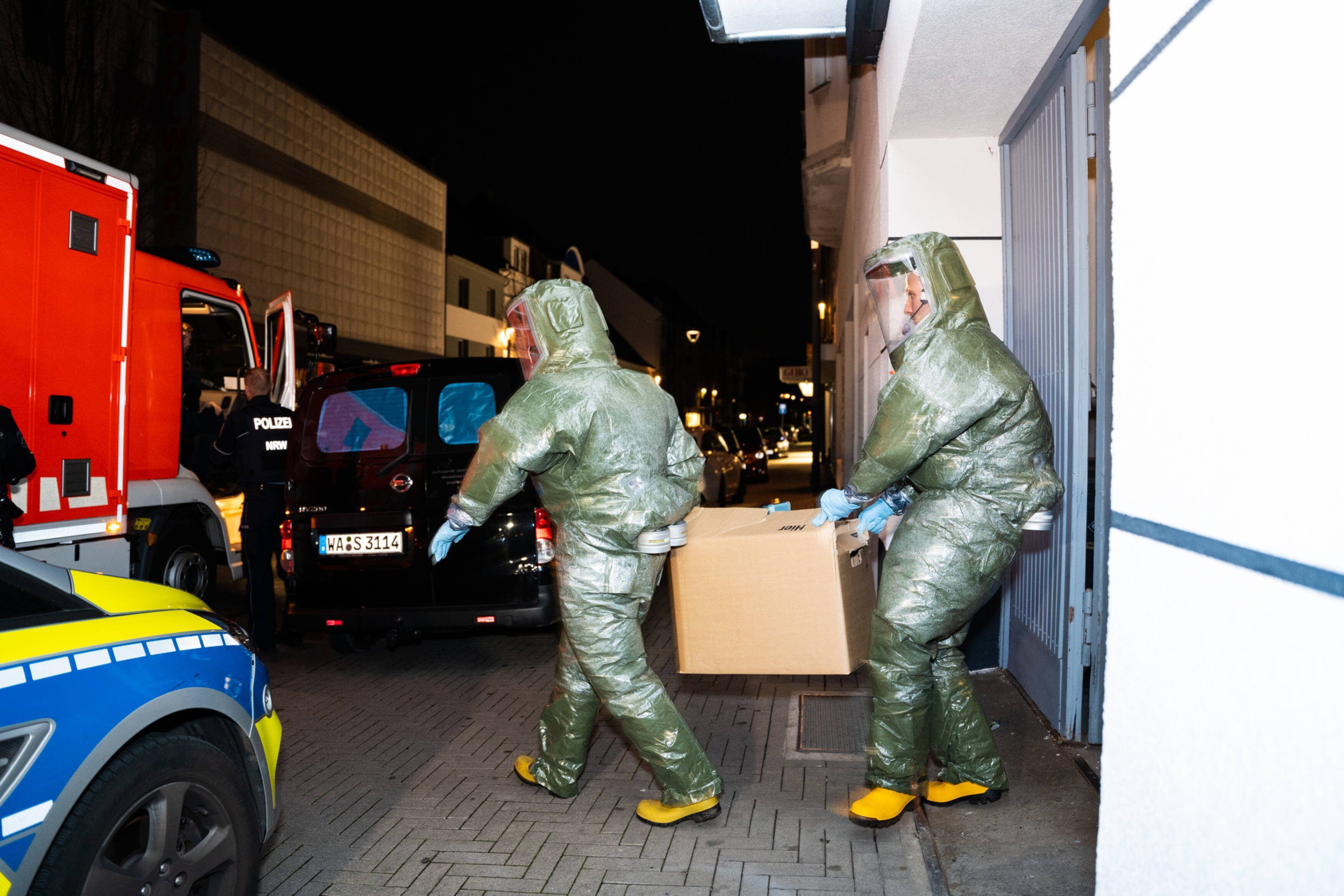 Männer in Schutzanzügen tragen einen Karton aus dem Haus, in dem ein Anti-Terror-Einsatz stattfand.