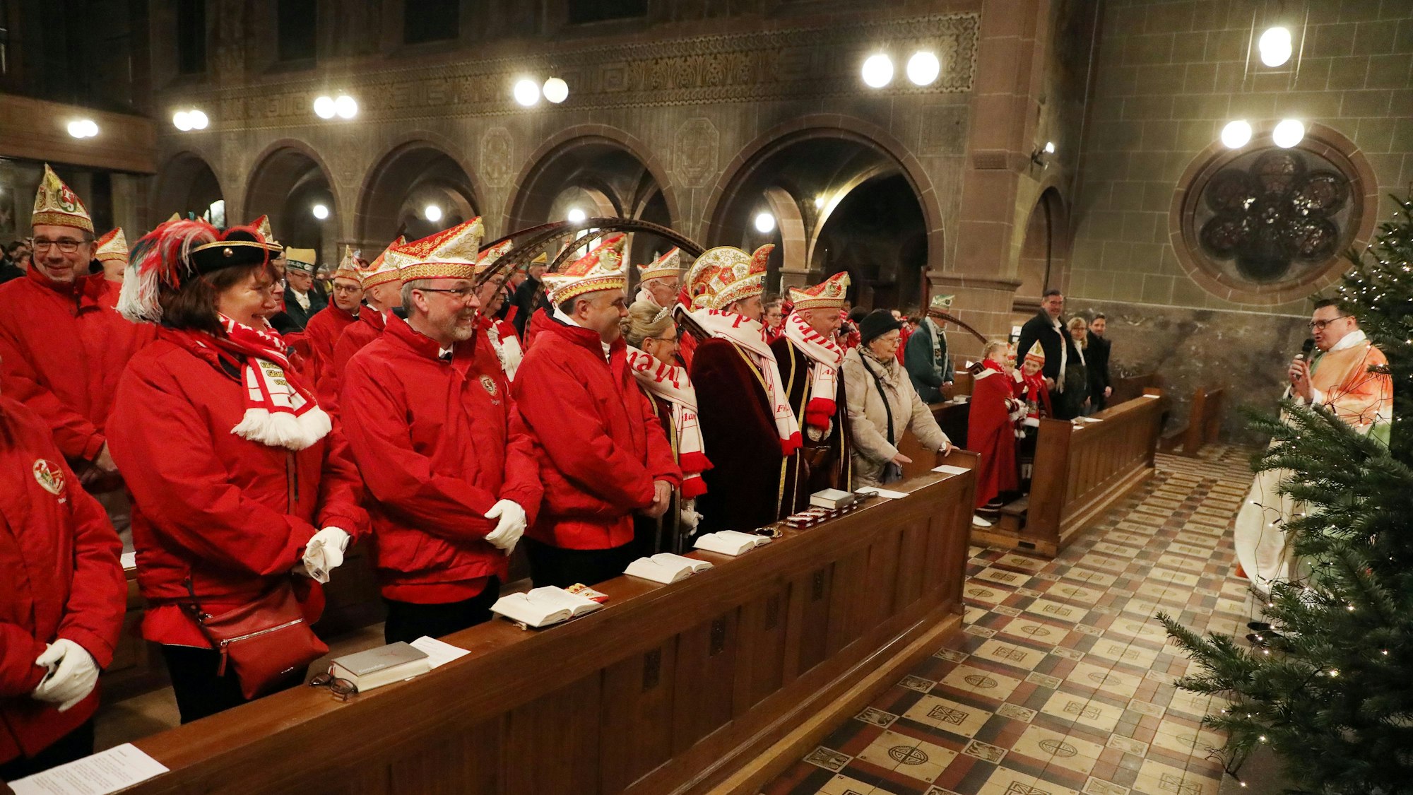 In der Kirche sitzen mit roten Jacken und Narrenkappen bekleidet Bergisch Gladbacher Karnevalisten, vorne redet Kreisdechant Norbert Hörter.