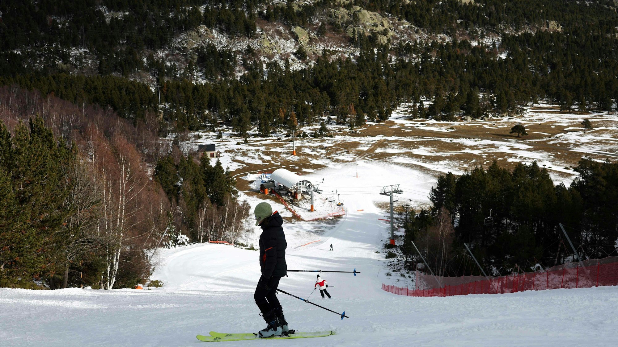Es ist ein Skifahrer zu sehen, der auf der Piste steht und bergab schaut.
