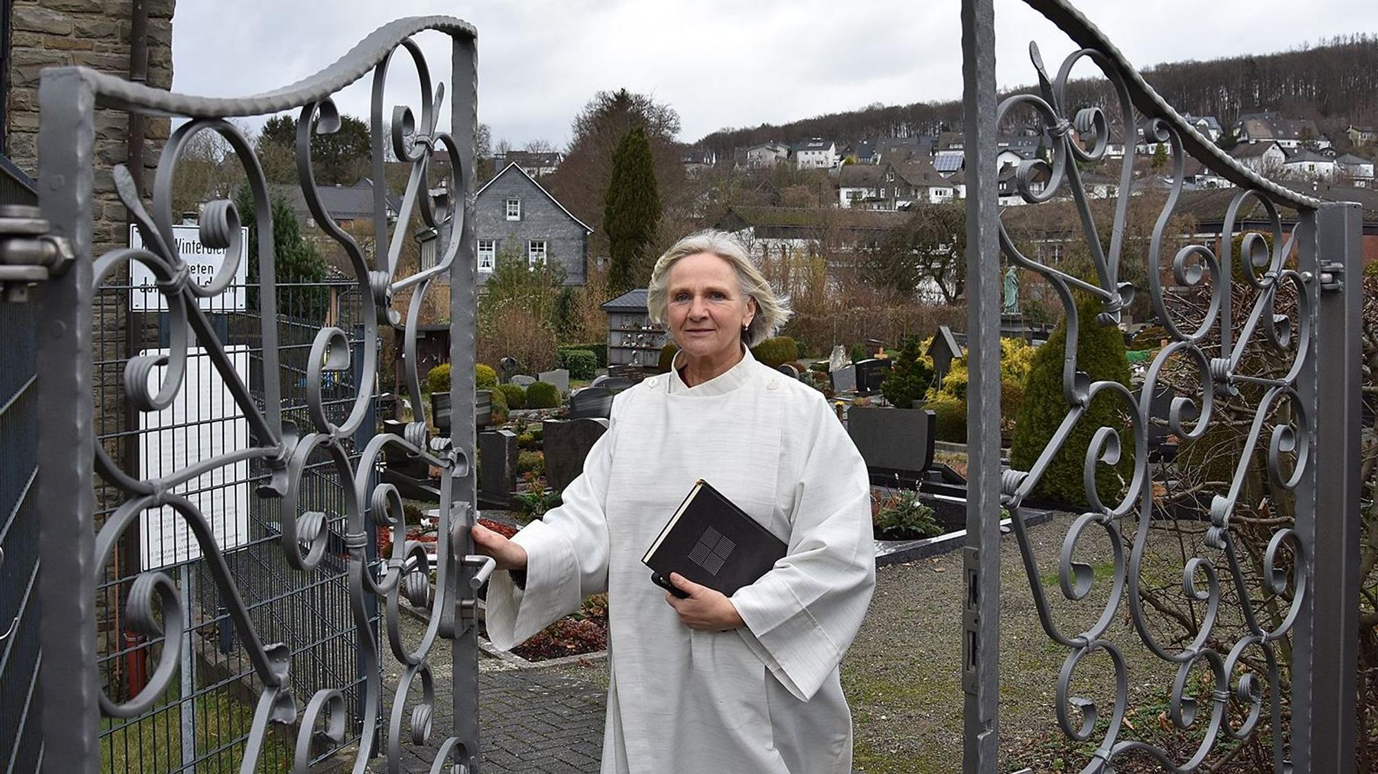 Mechthild Heide steht an einem Friedhofstor.