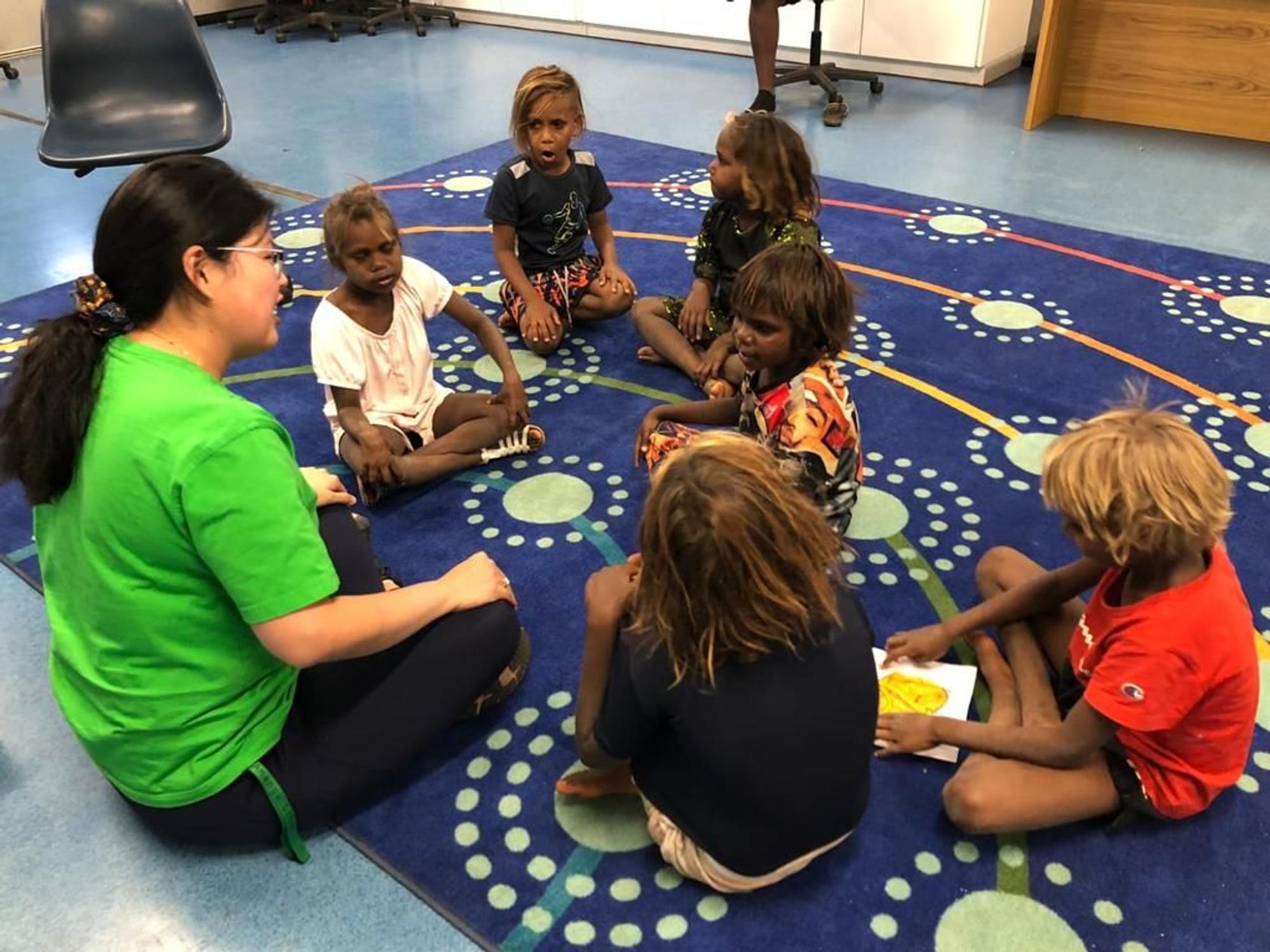Joyce Kee sitzt mit Kindern in einem Proberaum in Australien und bringt ihnen Singen bei.