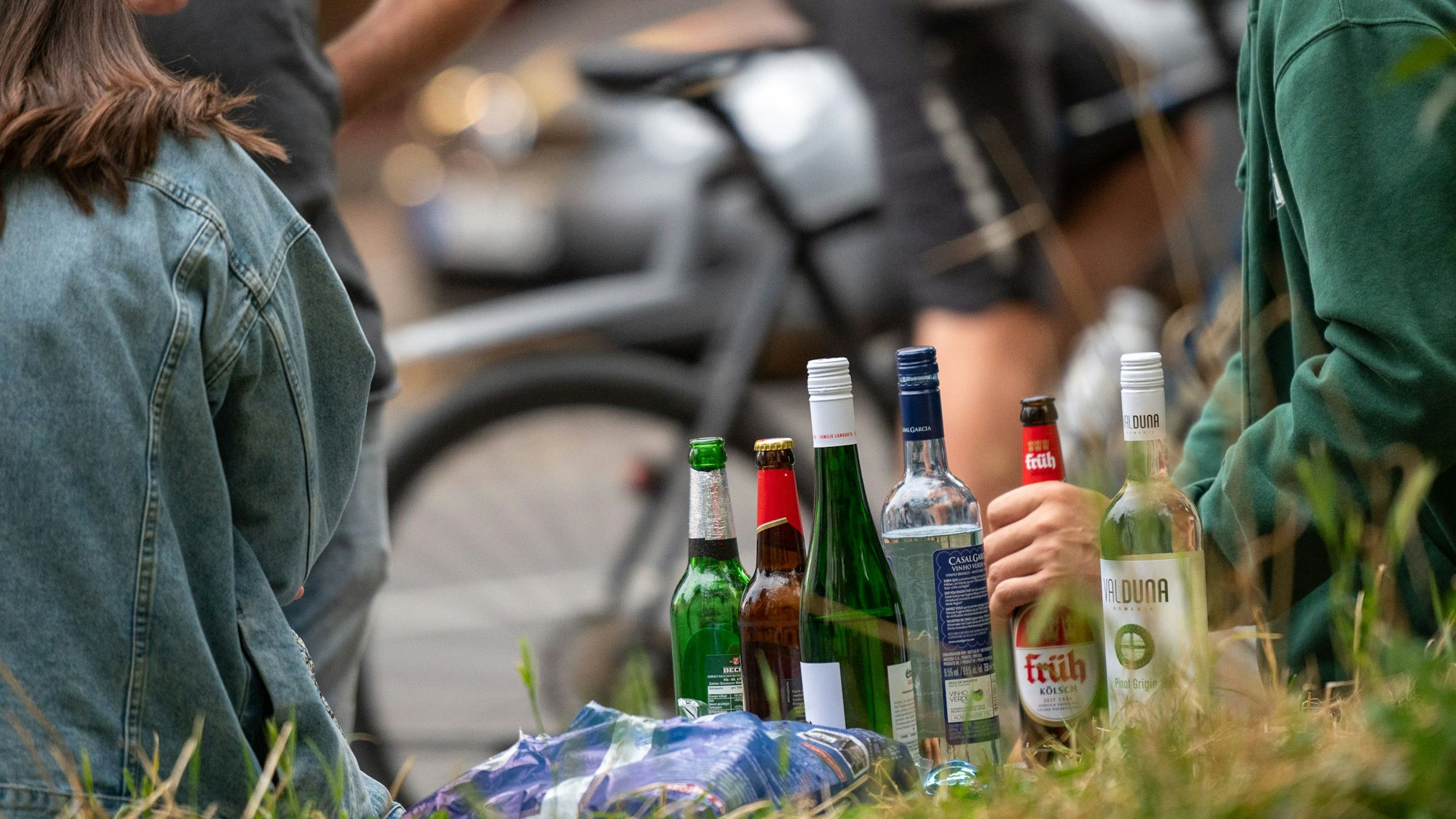 Zwei Personen sitzen auf einer Mauer, mit dem Rücken zur Kamera, zwischen ihnen diverse alkoholische Getränke in Glasflaschen.