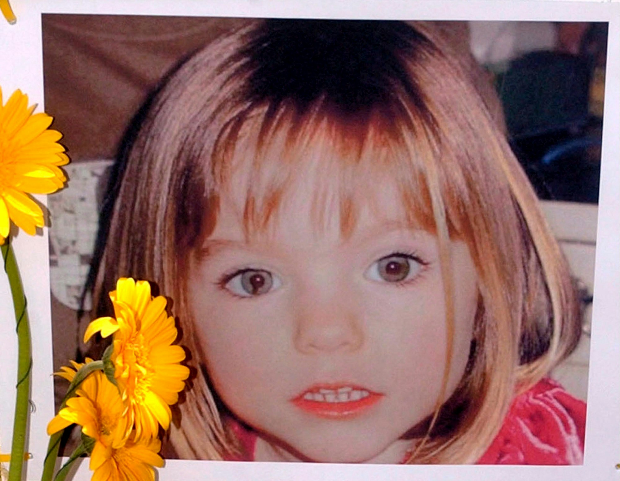 ARCHIV - 12.05.2007, Portugal, Lagos: Blumen stehen vor einem Bild, das die verschwundene Madeleine McCann (Maddie) auf einem Foto zeigt, das ihre Eltern im Zusammenhang mit dem Verschwinden des Kindes veröffentlich haben.
