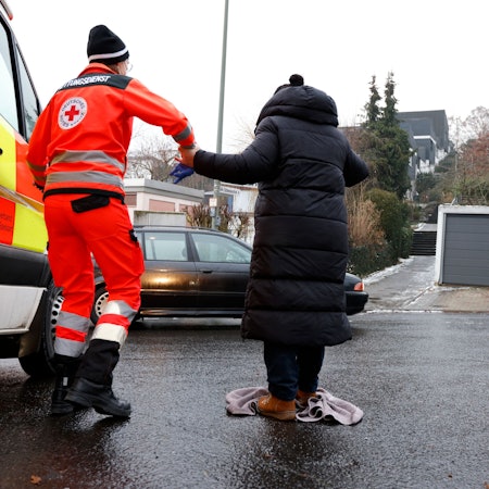 Der Rettungsdienst hilft einer Dame bei Glätte über die Straße.
