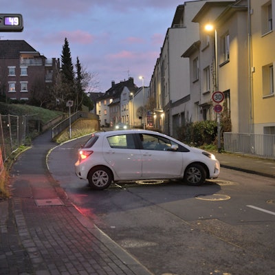Ein weißer Kleinwagen steht quer auf der Straße vor dem Parkhaus des Bergisch Gladbacher Marienkrankenhauses.