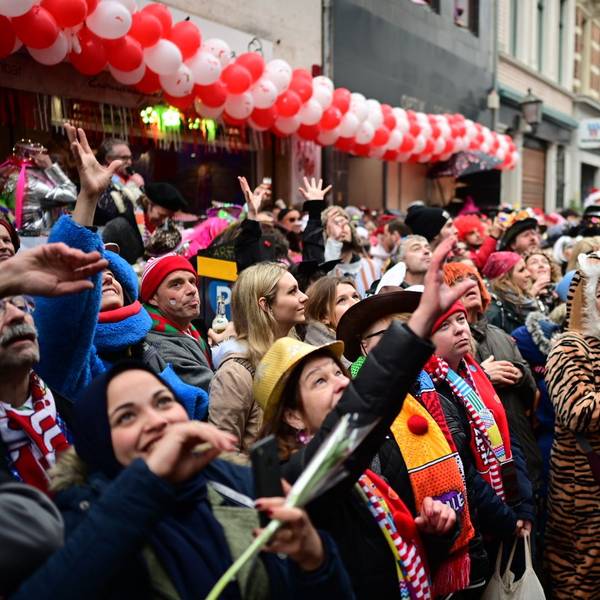 Bunt verkleidete Menschen jubeln an Rosenmontag 2020 einem Wagen des Rosenmontagszugs zu. Sie heben die Hände und sind gut gelaunt.