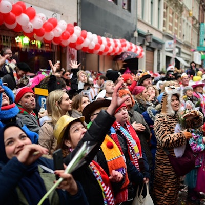 Bunt verkleidete Menschen jubeln an Rosenmontag 2020 einem Wagen des Rosenmontagszugs zu. Sie heben die Hände und sind gut gelaunt.