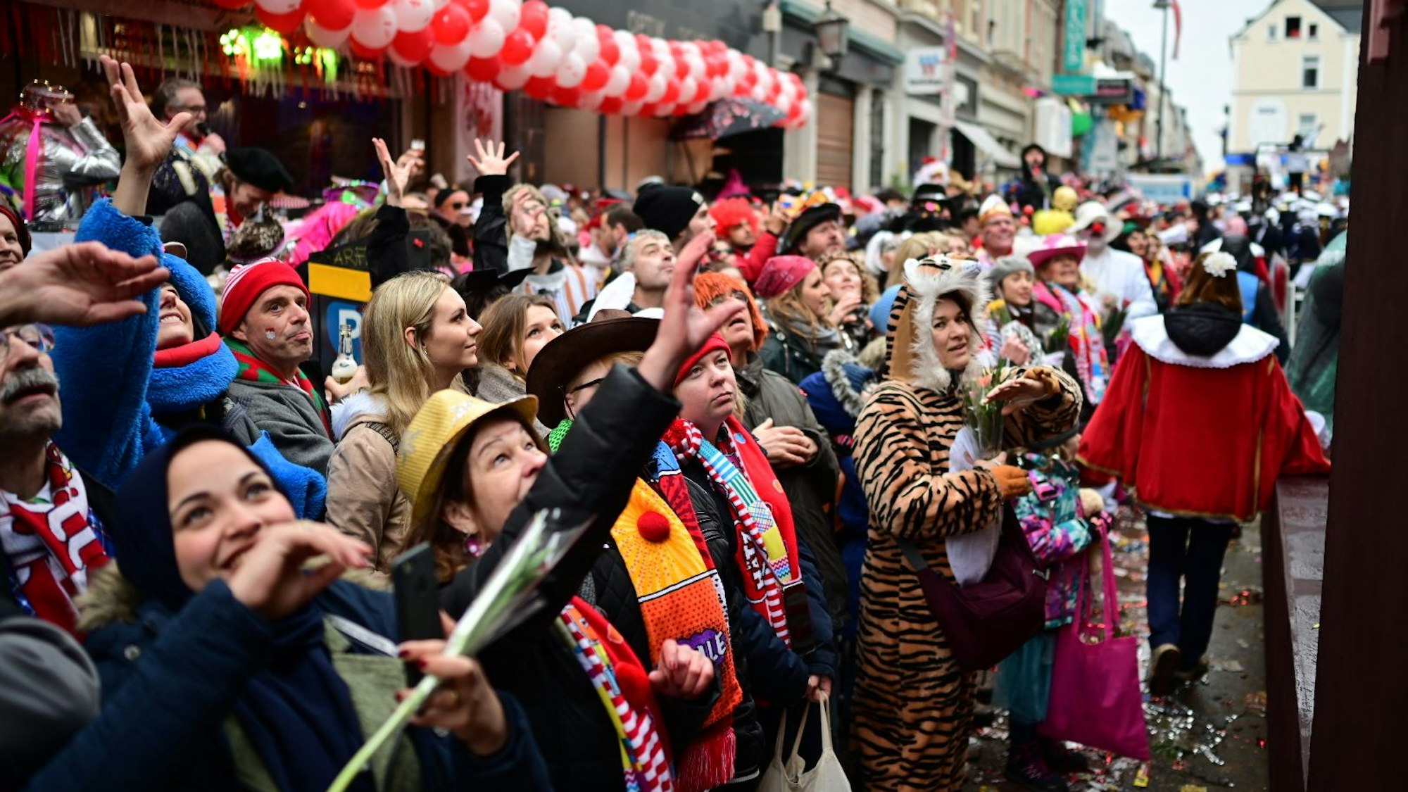 Bunt verkleidete Menschen jubeln an Rosenmontag 2020 einem Wagen des Rosenmontagszugs zu. Sie heben die Hände und sind gut gelaunt.