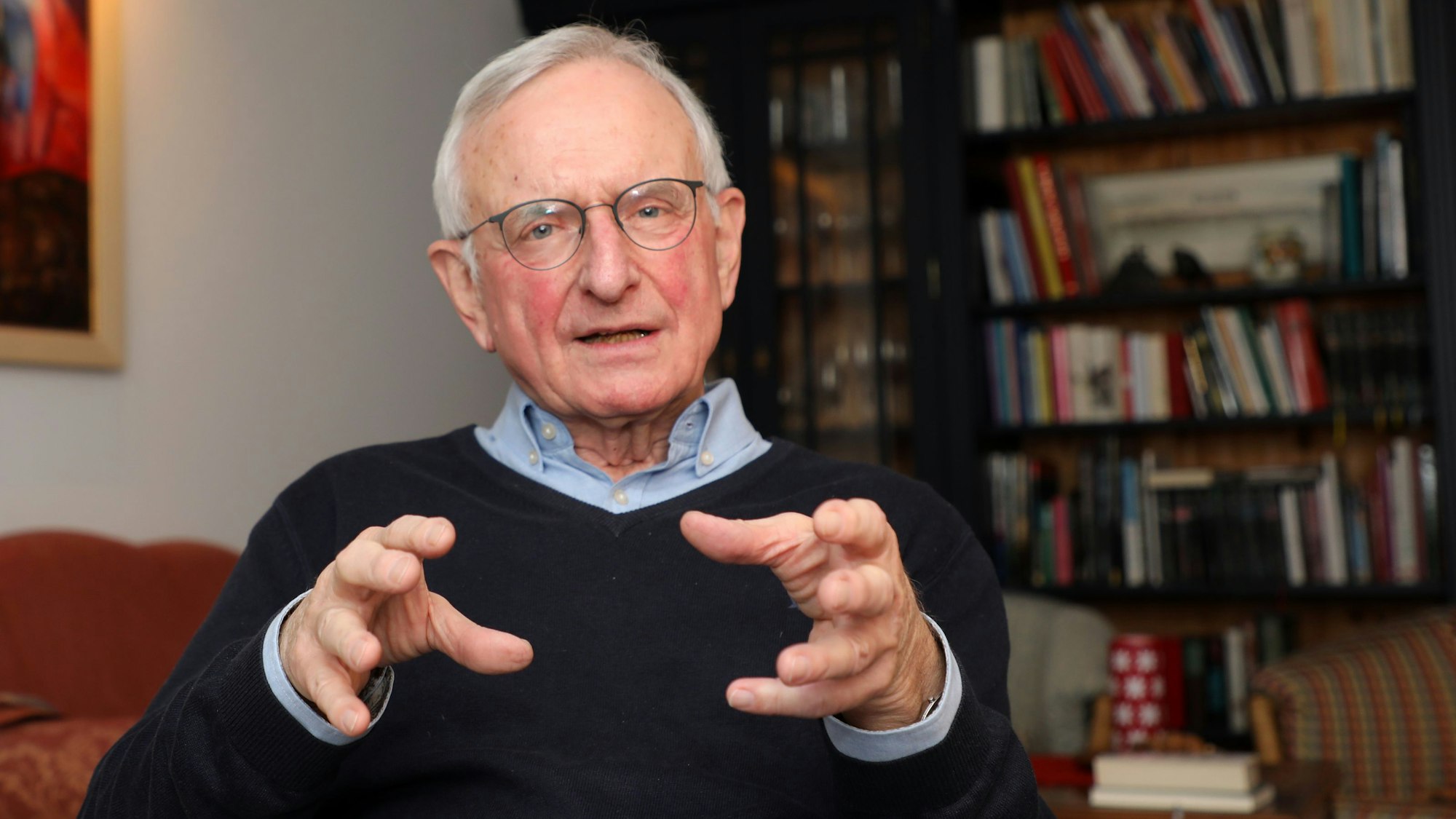 Der katholische Seelsorger Heinz-Peter Janßen sitzt im Wohnzimmer seines Hauses in Bergisch Gladbach-Herkenrath vor einer Bücherwand und spricht.