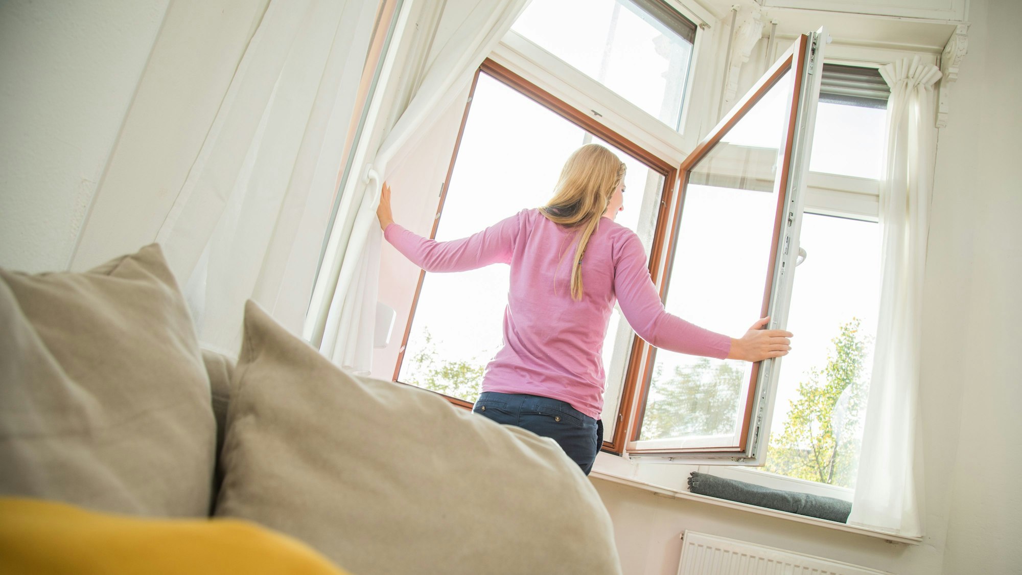 Eine Frau öffnet das Fenster, um ihre Wohnung zu lüften.