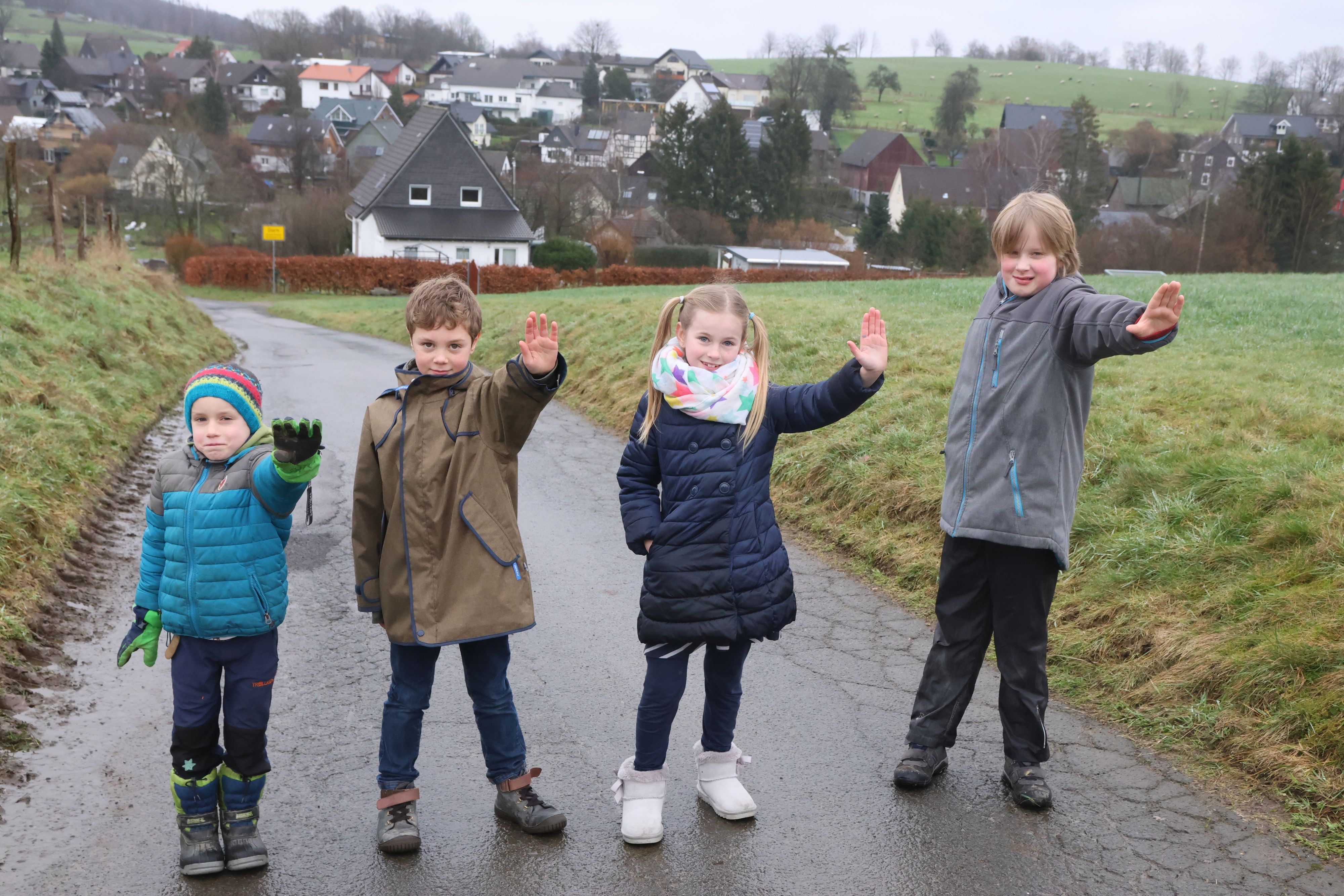 Man sieht die Kinder, wie sie nebeneinander auf dem Feldweg stehen, sie strecken jeweils ihre linke Hand als Stop-Signal nach vorne.