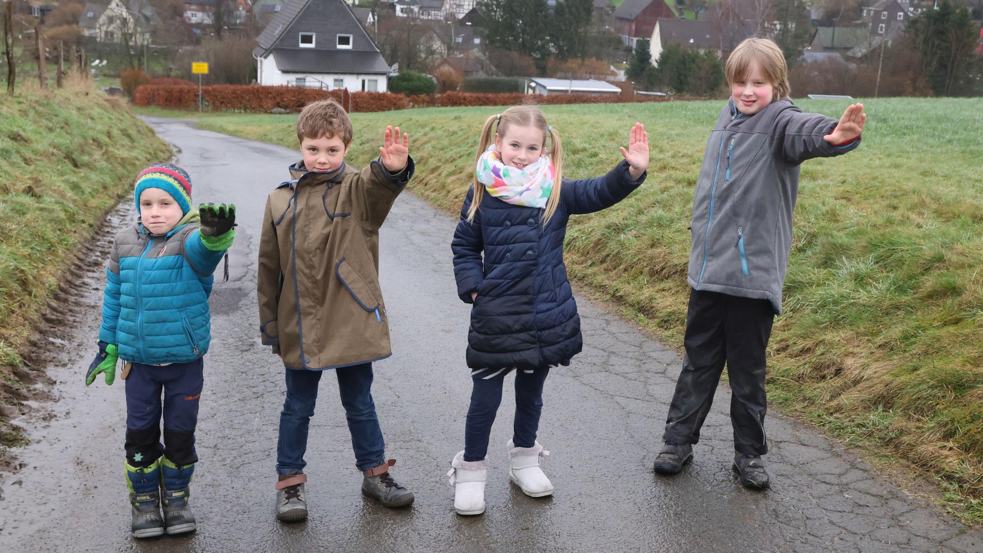 Man sieht die Kinder, wie sie nebeneinander auf dem Feldweg stehen, sie strecken jeweils ihre linke Hand als Stop-Signal nach vorne.