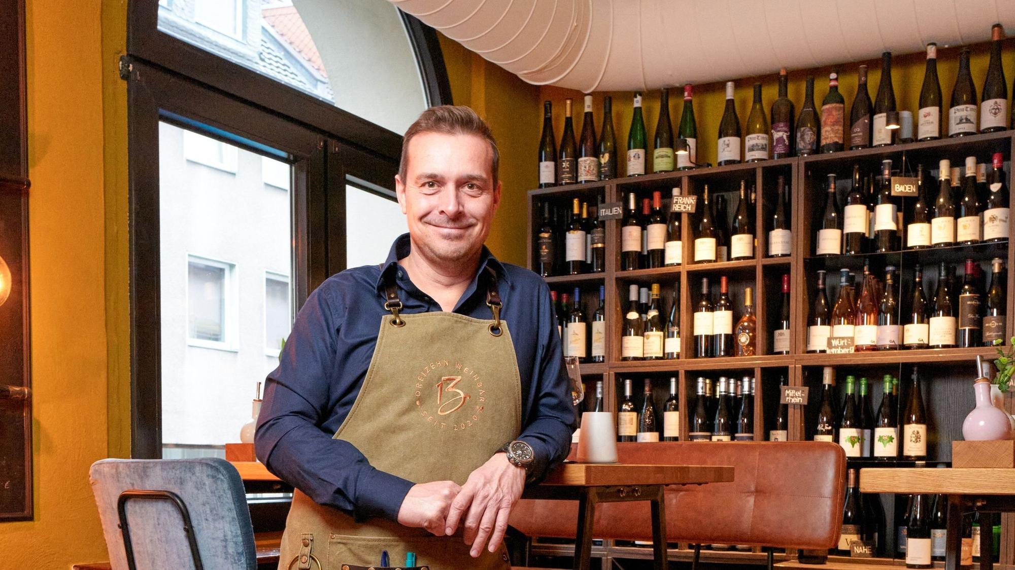 Mann mit Schürze steht vor einem Regal mit Weinflaschen