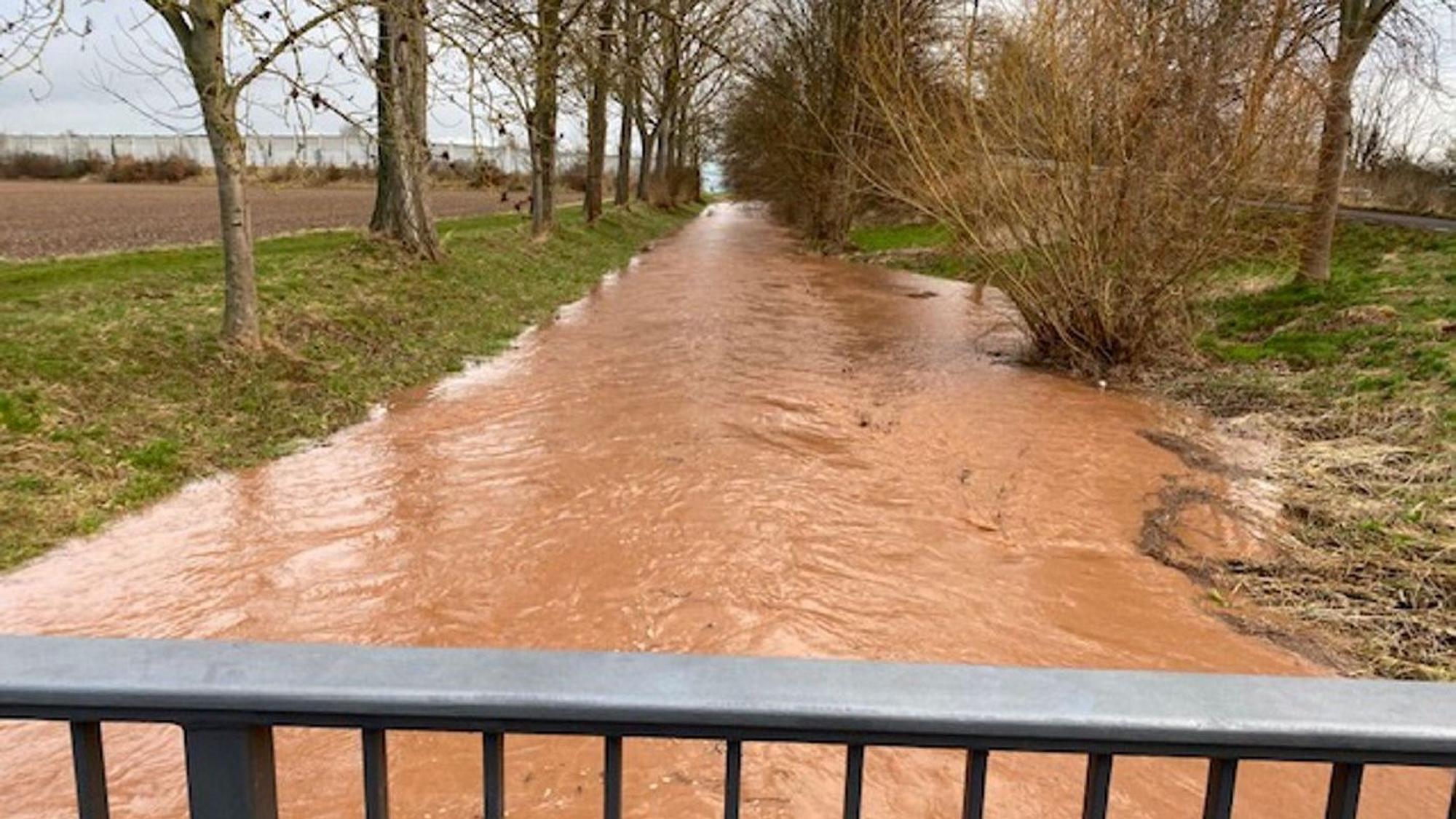 Zu sehen ist ein breiter Strom von Wasser, Blick von der Brücke. Das Wasser ist schlammbraun.