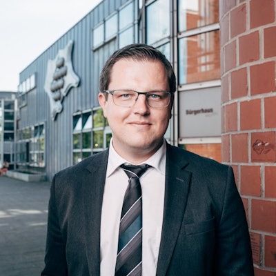 Matthias Neugebauer steht vor dem Stadthaus der Stadt Hürth. Er trägt Anzug und Brille.