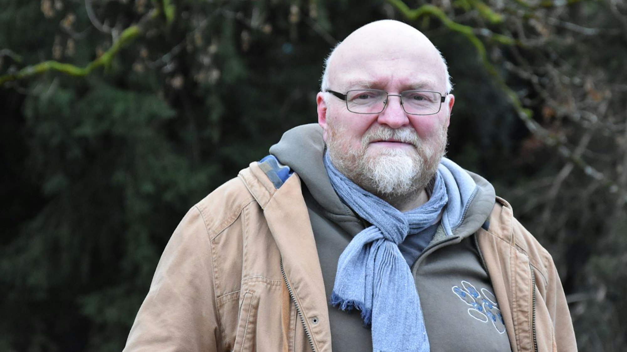 Man sieht Pedall vor einem Wald im Hintergrund stehen. Er schaut in die Kamera.