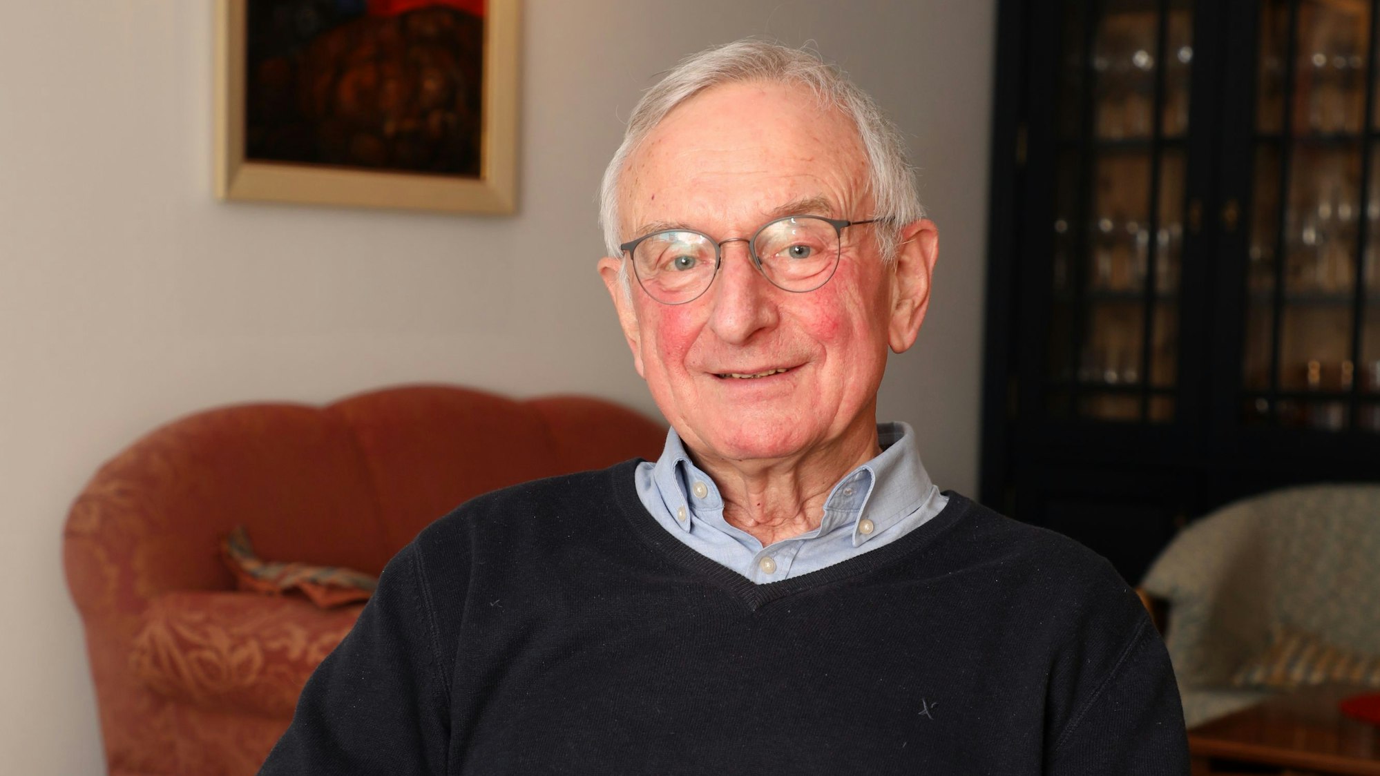 Man sieht den Pfarrer in einem Raum, er sitzt und schaut in die Kamera.