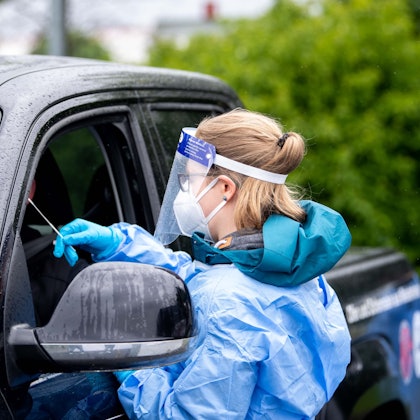 Eine Mitarbeiterin eines Corona-Testzentrums trägt Schutzkleidung und führt bei einem Autofahrer einen Test durch.