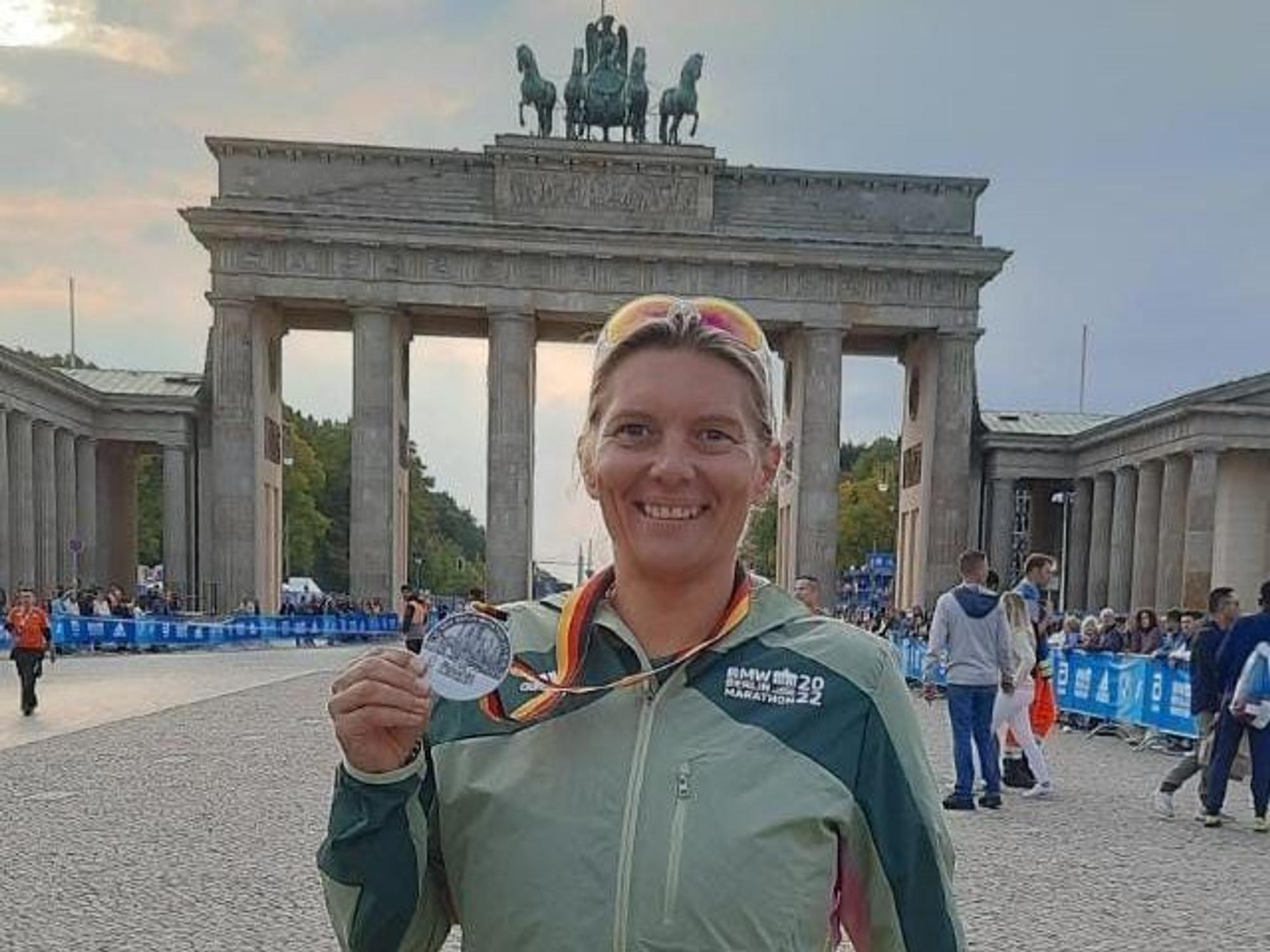 Ilona Schaffrath steht in Sportkleidung und mit einer Medaille um den Hals vor dem Brandenburger Tor.