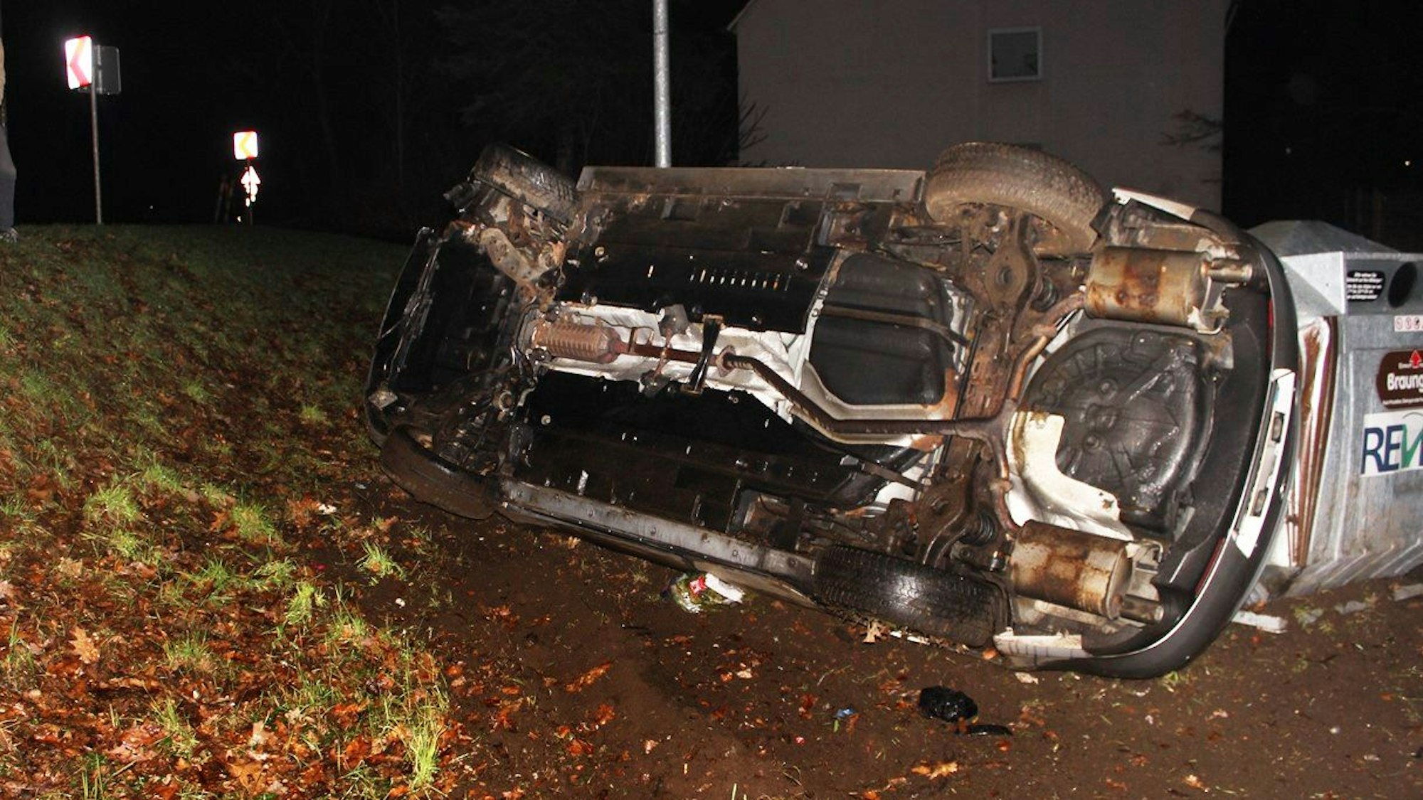 Ein Auto liegt auf der Beifahrerseite neben eine Glascontainer.
