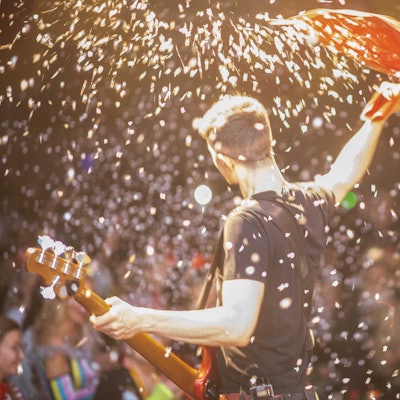 Ein Musiker mit Bassgitarre steht im Konfettiregen auf der Bühne.