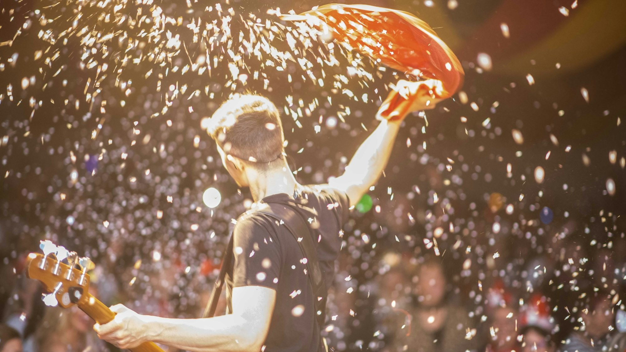 Ein Musiker mit Bassgitarre steht im Konfettiregen auf der Bühne.