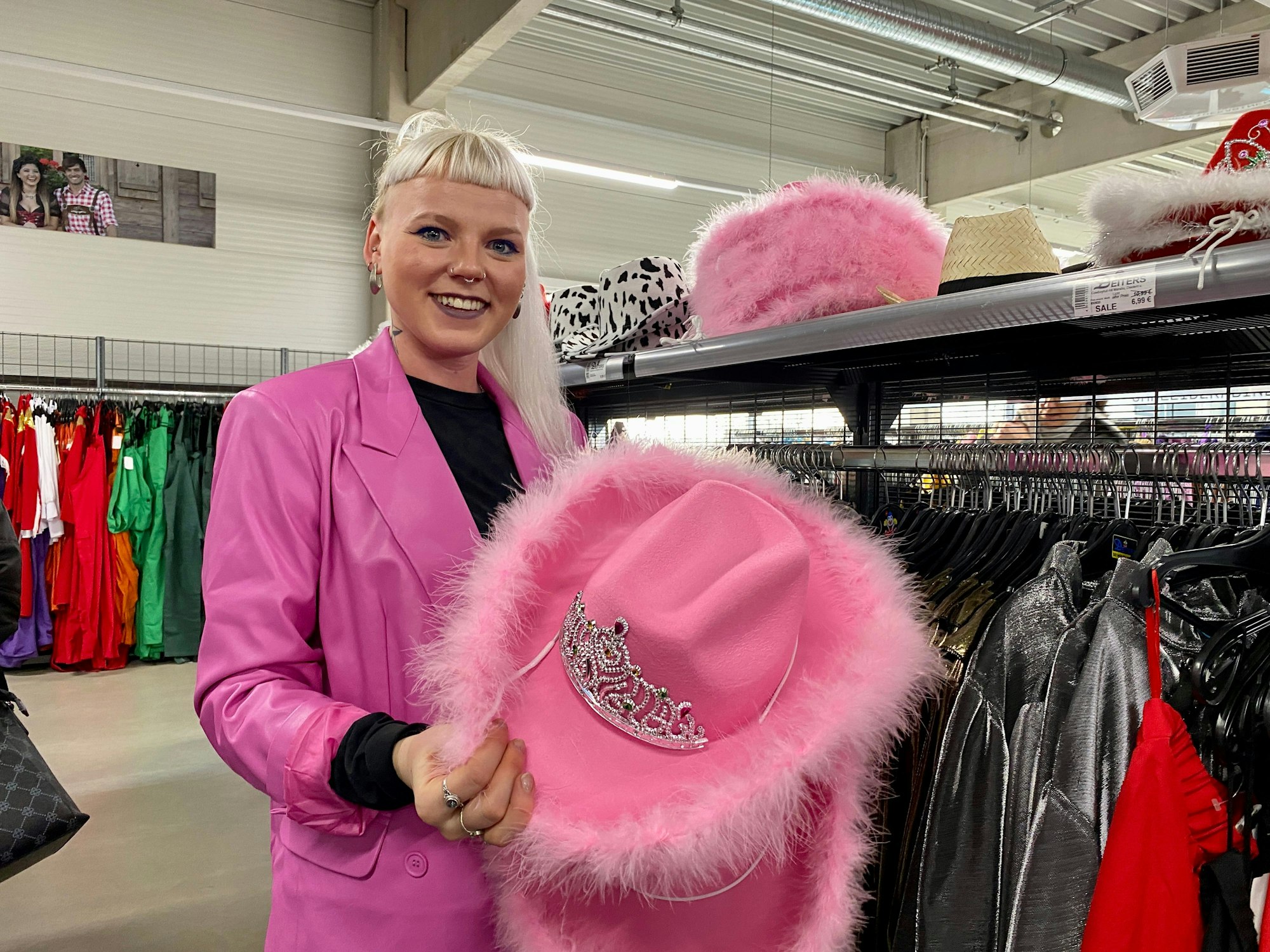 Eine Frau im pinken Anzug hält einen rose Cowgirlhut, der mit Glitzer versehen ist.