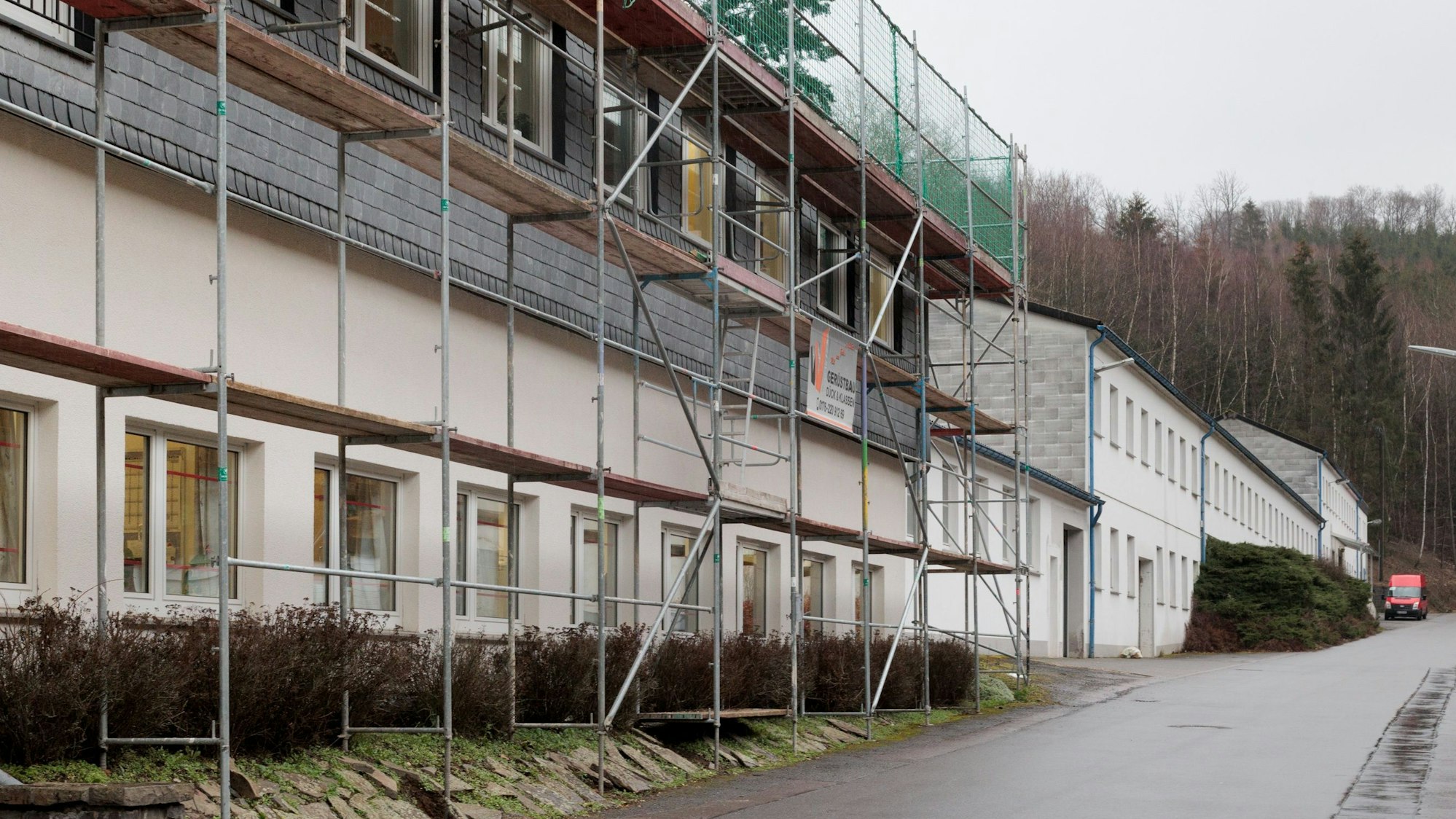 Vor einer Hausfassade an einer langgezogenen Straße steht ein Baugerüst.