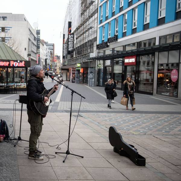 Ein Straßenmusiker spielt in der Fußgängerzone auf seiner Gitarre und singt.