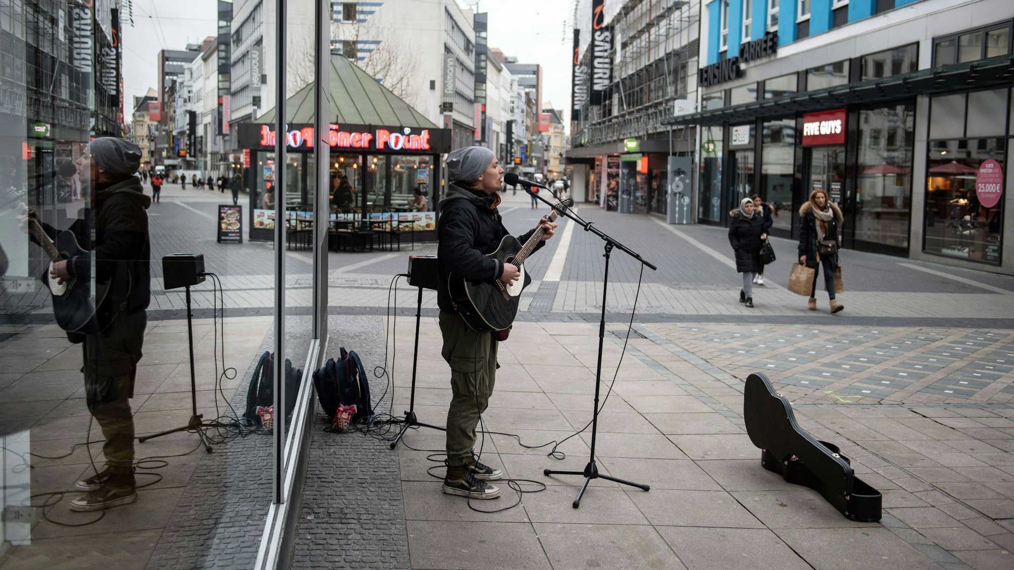 Ein Straßenmusiker spielt in der Fußgängerzone auf seiner Gitarre und singt.