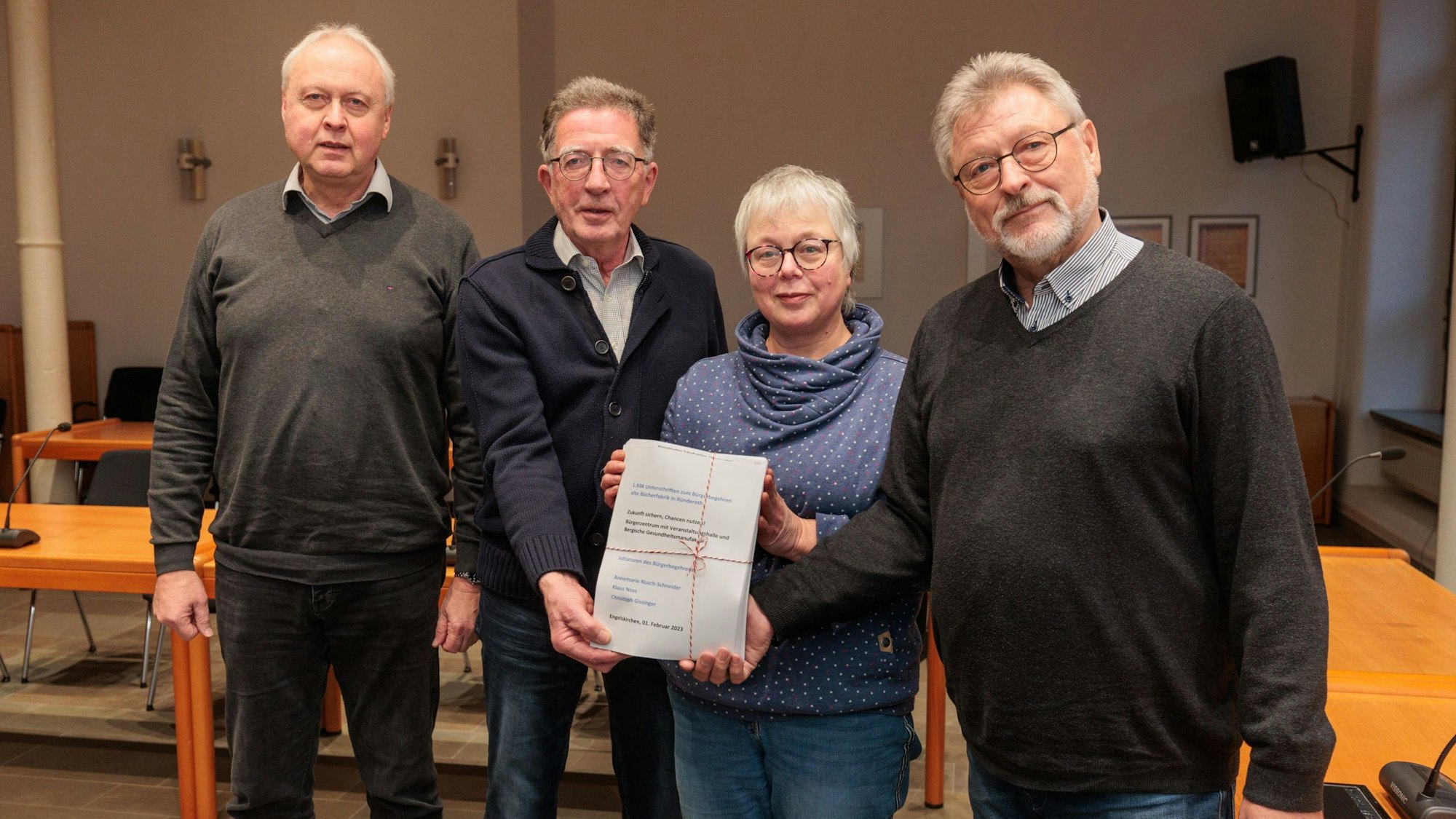 Drei Männer und eine Frau stehen nebeneinander und halten eine Unterschriftenliste in die Kamera.