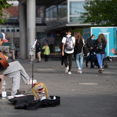Die Stadt Bergisch Gladbach hat Verstärker für Straßenmusiker verboten. Ein Straßenmusiker sitzt mit Gitarre in einer Fußgängerzone.