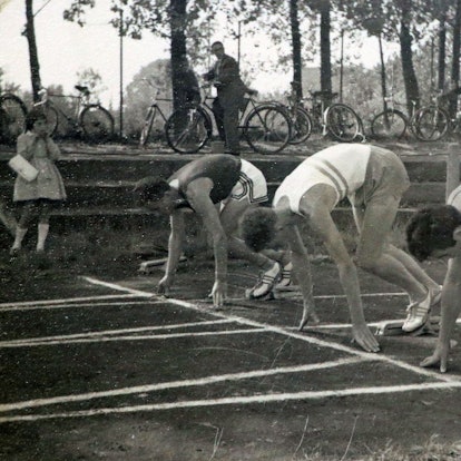 Athleten an der Startlinie auf einer Laufbahn. Das Bild ist in schwarz-weiß.