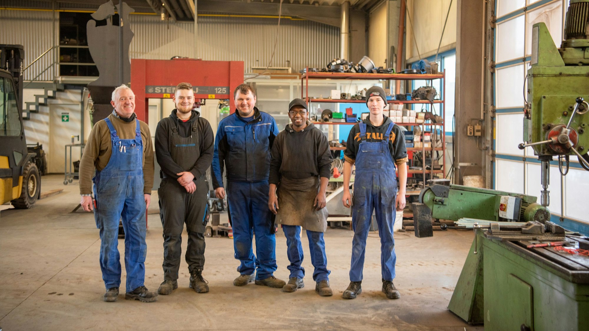 Hady Bah steht zwischen vier seiner Kollegen in der Metallwerkstatt.