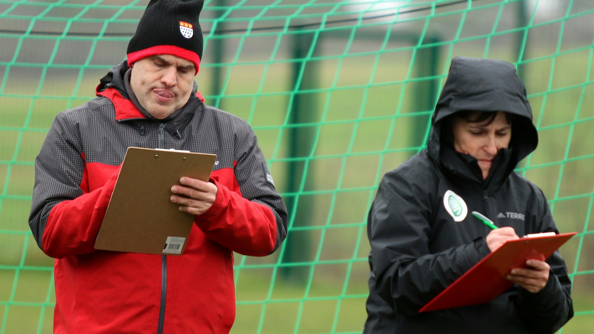 Zwei Teilnehmer des Lehrgangs stehen mit Kugelschreiber und Klemmbrett vor einem Tor und schreiben mit.
